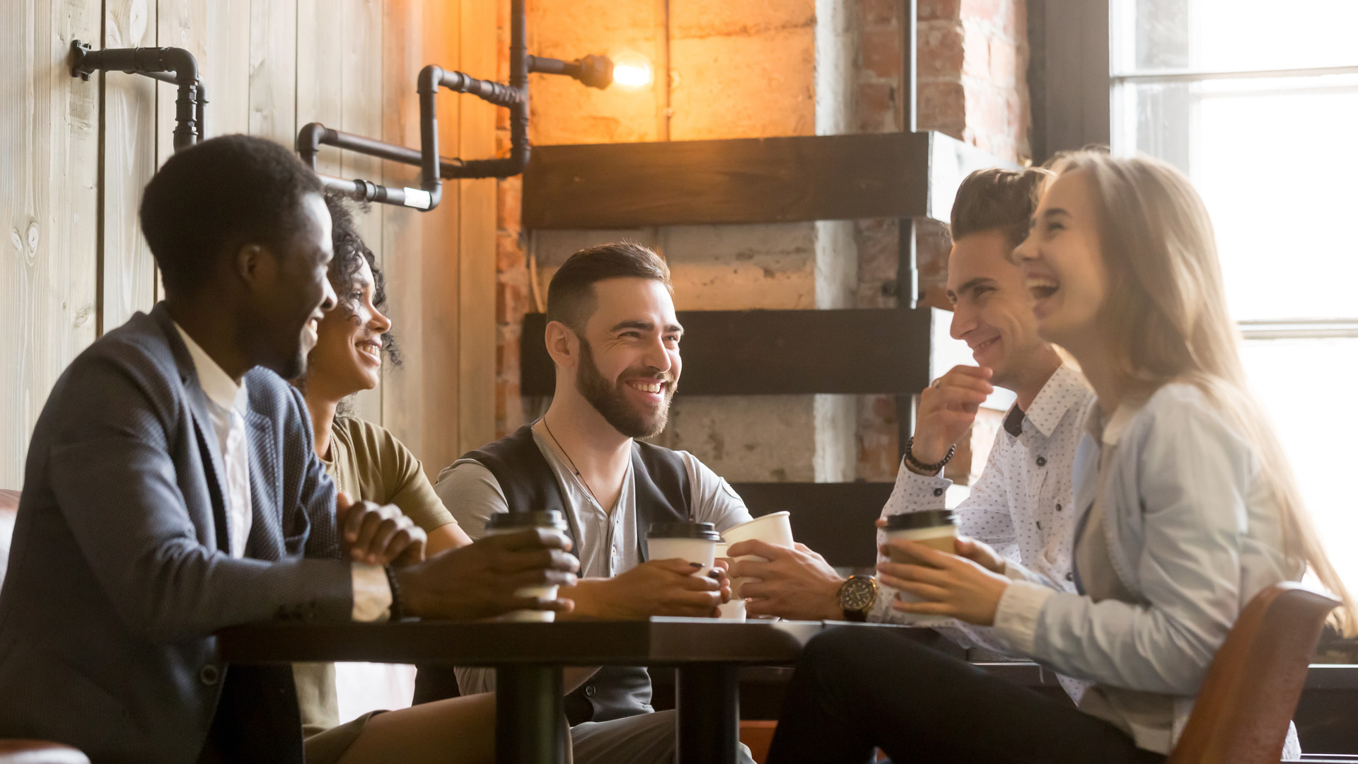 Multiracial friends having fun and laughing drinking coffee in coffeehouse
