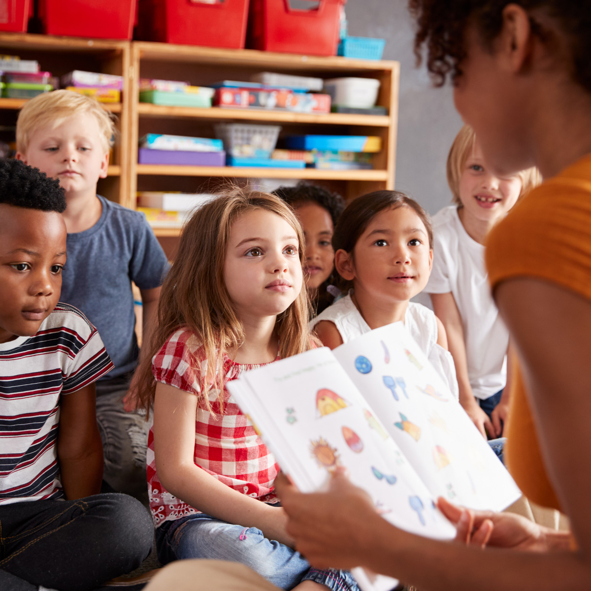 Group Of Elementary School Pupils Sitting On Floor Listening To Female Teacher Read Story