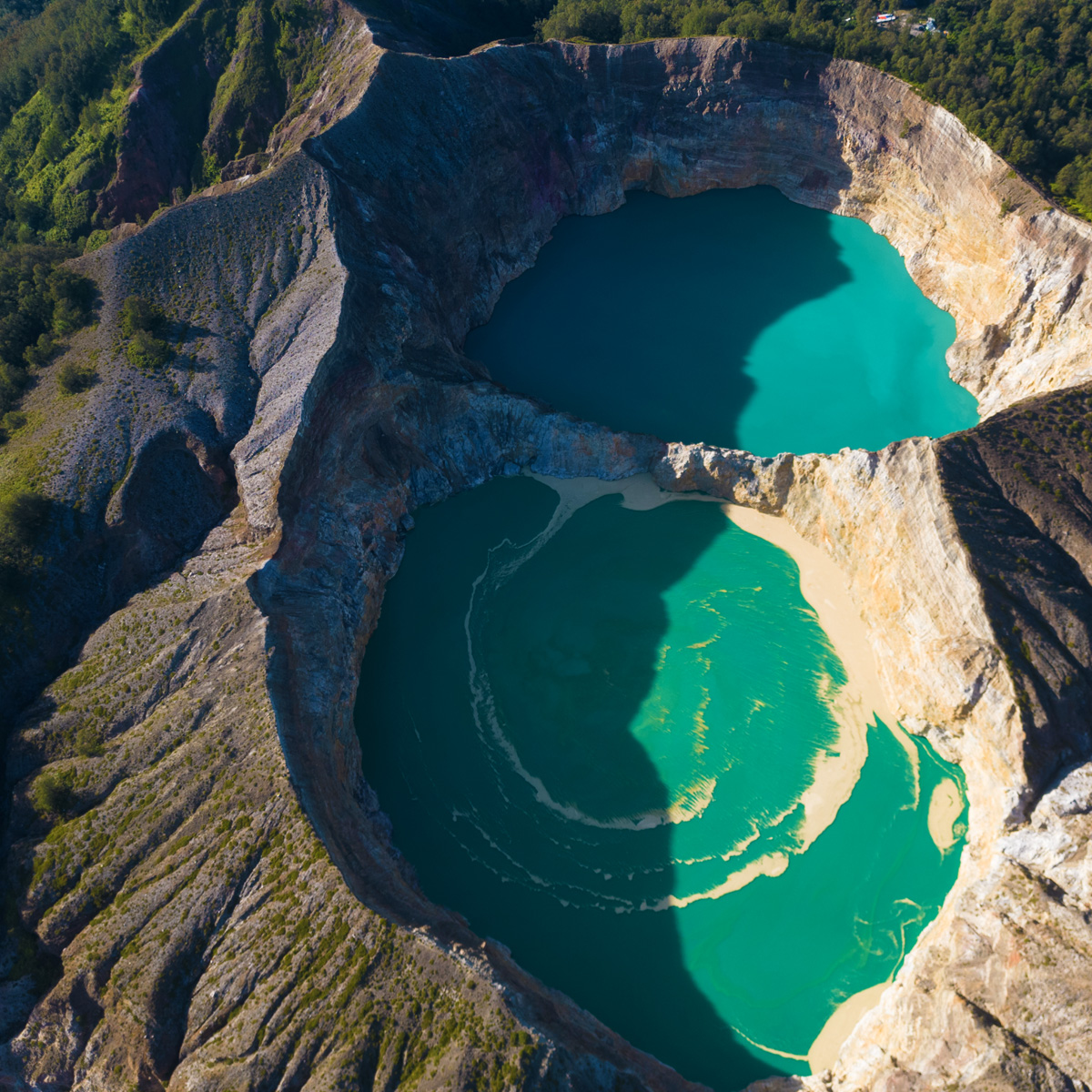 Aerial view of vibrant turquoise crater lakes surrounded by lush terrain.