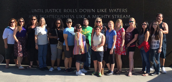 Photo of Service Learning Center students in front of wall that says "Until justice rolls down like waters and righteousness like a mighty stream". 