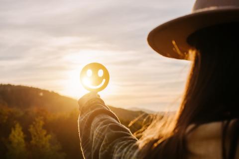 Close up of young woman holding happy smile face on background epic sunset in mountains at autumn sunny day