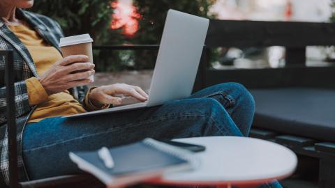 Person sitting outside using a laptop and drinking coffee