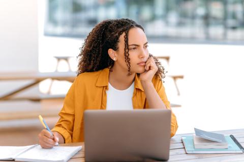 Woman sitting in front of a laptop thinking
