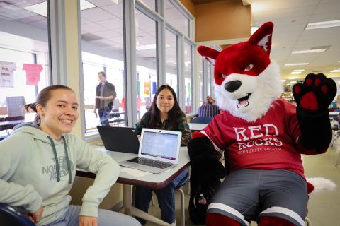 two students sitting with the college mascot Copper