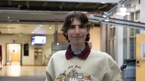 Alexei, a student, stands in a hallway smiling.