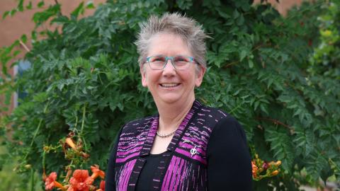 Woman looks at the camera and smiles in front of a tree