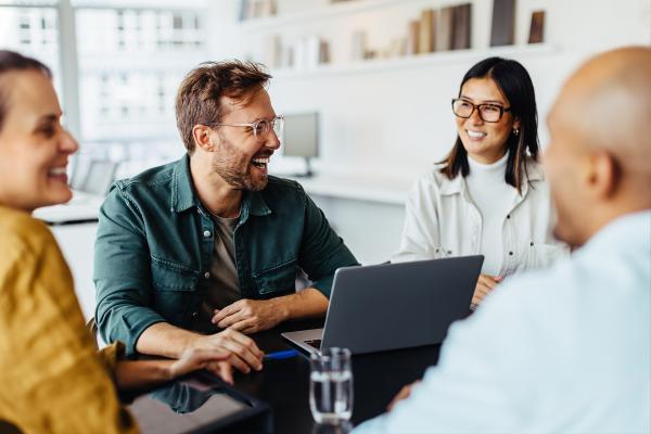 Business people sitting around a table using a laptop and laughing