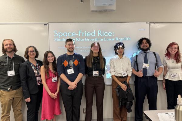 A group of people pose smiling in front of a slide projection that says Space-Fried Rice