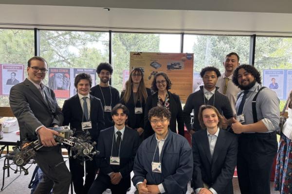 Students in suits pose while holding a robotic rover