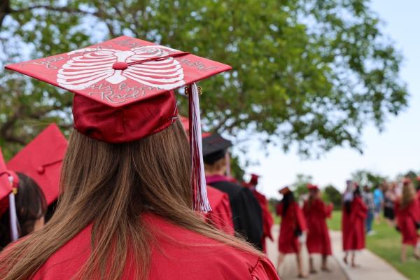 Graduates in red caps and gowns lined up and walking away on a lawn.