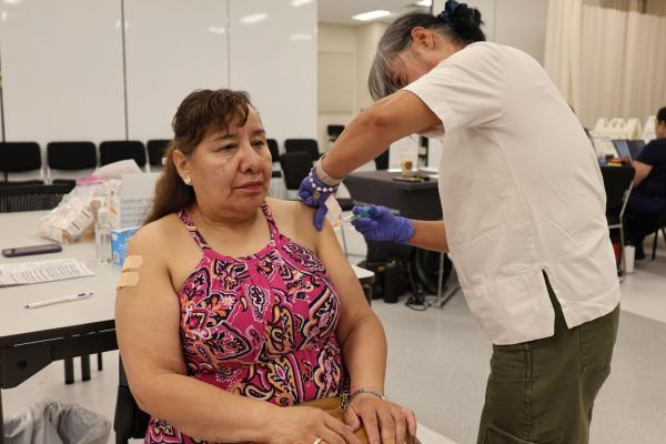 A woman is on a chair while a nurse is giving her a vaccine.