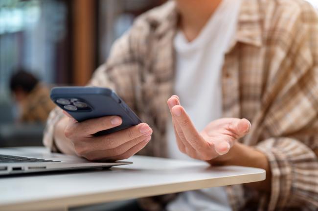 Close up of hands holding phone over laptop and talking or explaining sitting at cafe's table.
