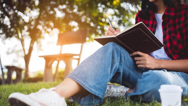student sitting in the grass writing
