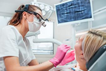 Dentist female doctor dressed uniform in magnifying glasses performing preventive dental care.
