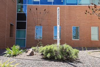 A white column with the words peace pole in a garden