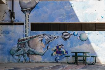 Wall with mural featuring face and clouds, in front of a bench.