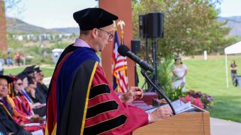 Side view of college President Dr. Landon Pirius at the podium wearing regalia