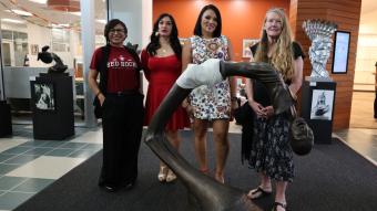 Four women stand behind a sculpture of Ghandi