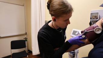 An RRCC student in black scrubs listens closely on a stethescope as she takes a person's blood pressure.