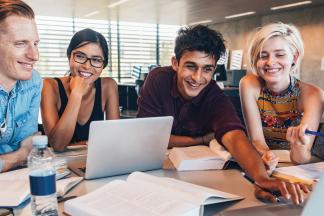 Group of people smiling, sitting around a table using a laptop