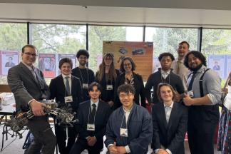 Students in suits pose while holding a robotic rover