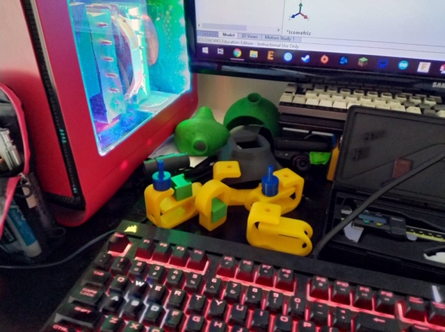 Green and yellow 3D printed plastic pieces next to computer. 